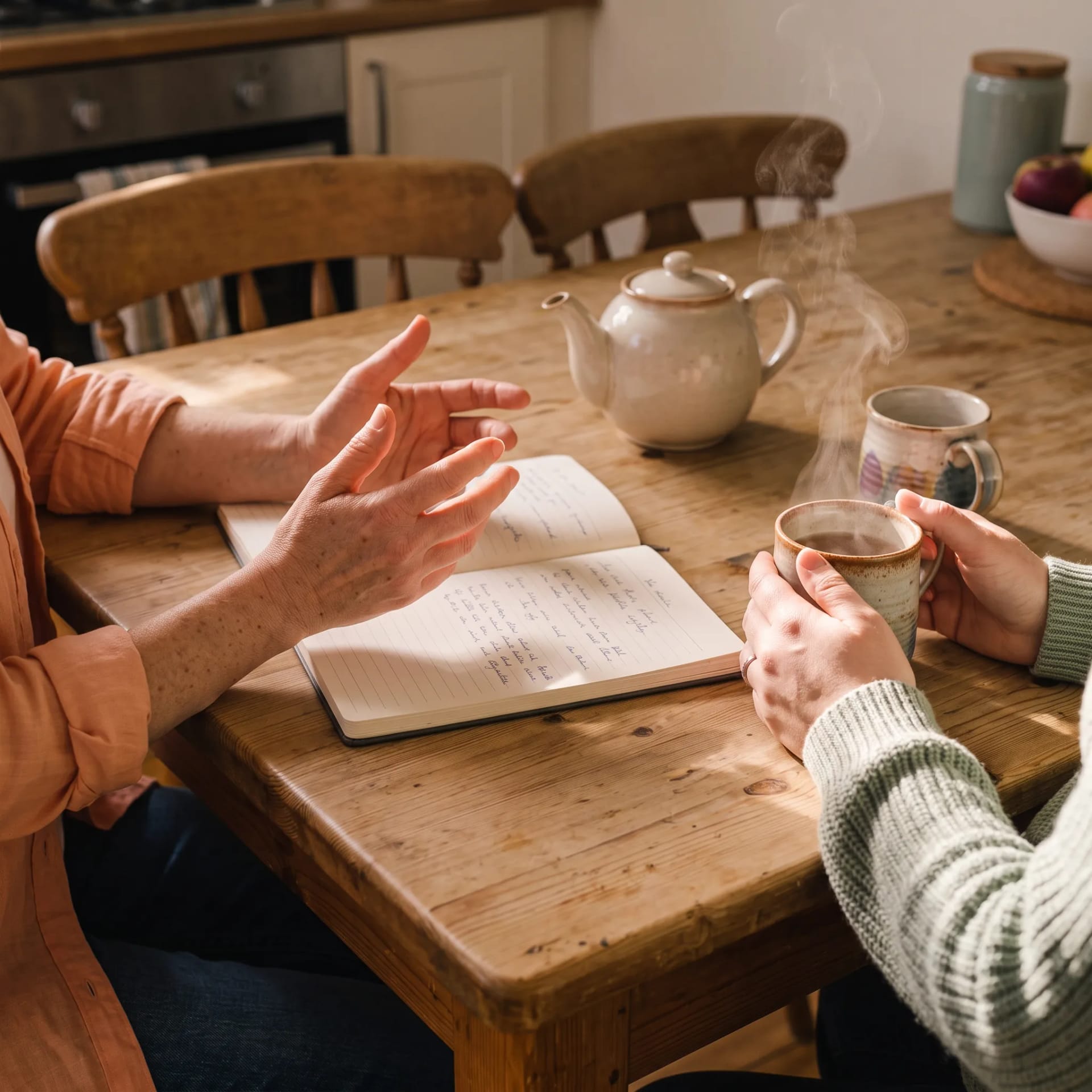 Tea, a birth-plan notebook and two pairs of hands on a kitchen table during a Peony Birth planning visit in Brighton